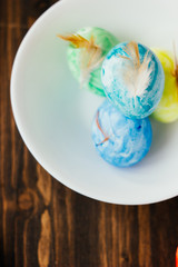 Blue, yellow and green color easter eggs on ceramic bowl over rustic table.