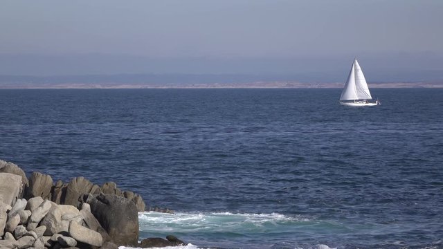 Vast open ocean water with sailboat in distance floating on waves.