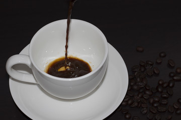 Pour hot coffee into a cup of white on a dark background.