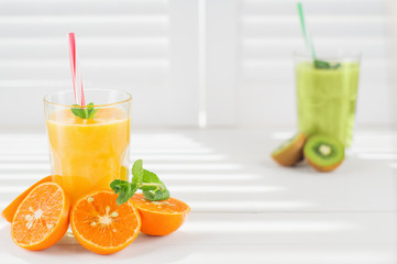 Fresh orange juice and kiwi juice. Freshly blended fruit smoothies in glasses on a white wooden background. Fresh fruit cocktails. Diet concept. 