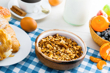 Breakfast made of oatmeal granola, croissants, milk, eggs, coffee and fruits on a table. Delicious healthy food.