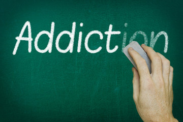 Hand erasing the word ADDICTION written on blackboard