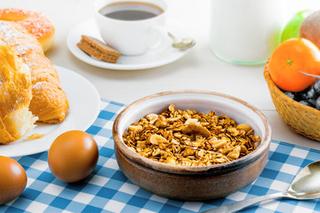 Granola, croissant, eggs, milk and fruits on a table. Healthy breakfast with coffee. International vegetarian meal.