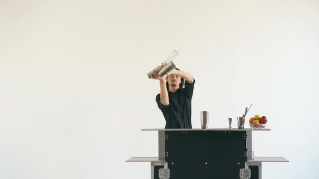 Professinal bartender man juggling bottles and shaking cocktail at mobile bar table on white background studio indoors