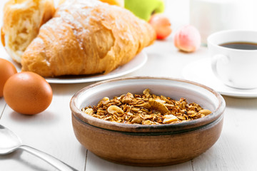 Oatmeal muesli with nuts, croissants, fruits, milk and coffee for delicious breakfast. Traditional healthy meal for breakfast on a table. Close-up.