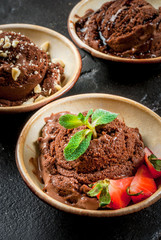 Three kinds of chocolate ice cream decoration: with chocolate sauce (syrup), with slices of strawberry and mint, with pieces of chopped nuts. On the black concrete stone table