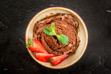Chocolate ice cream with pieces of mint and strawberry. On the black concrete stone table, top view copy space