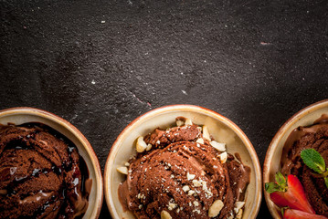 Three kinds of chocolate ice cream decoration: with chocolate sauce (syrup), with slices of strawberry and mint, with pieces of chopped nuts. On the black concrete stone table, top view copy space