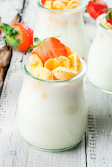 Summer light breakfast: homemade organic yogurt with cornflakes and fresh strawberries. On a white rustic wooden table copy space