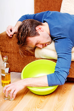 Drunk man sleeping on couch with whikey bottle and bowl