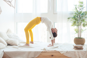 Female yogi makes a handstand at home on the bed.