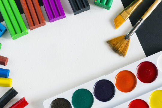 Watercolor paint, paint brushers, crayouns, plasticine on white paper over black background