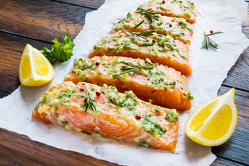 A process of cooking, pieces of raw salmon have been coated by garlic herb butter mixture on parchment paper, wooden table. - 139616681