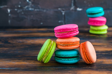 Colourful macaroons or macarons, pink, blue, green and orange ones on the dark wooden rustic table.