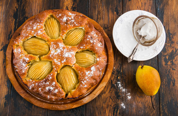 Italian round pear and chocolate cake on wooden rustic table, fresh fruits and icing sugar, top view.