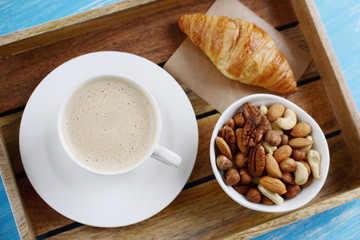 Cup of cappuccino, croissants and plate of nuts on the table