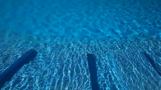 Sunlit swimming pool with clear blue water. Ripples on the water create beautiful movement.