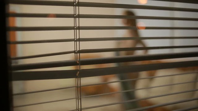 somebody spying on a girl from the street through the window blinds . crime