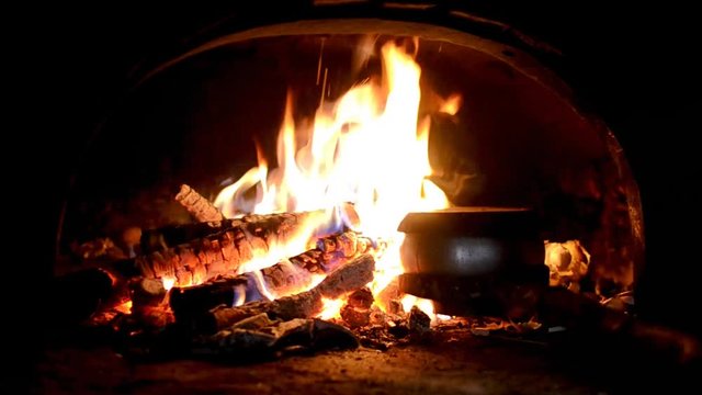 Man with the help of fork puts Cast-iron pot into the fire in the old traditional Russian village oven
