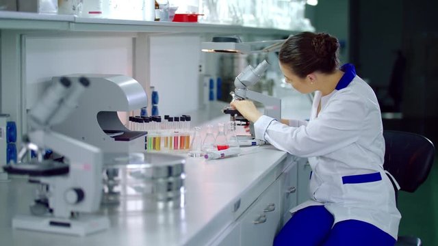 Lab researcher working with microscope in laboratory. Female researcher setting microscope in laboratory. Lab worker preparing microscope in lab. Woman scientist working with microscope in science lab