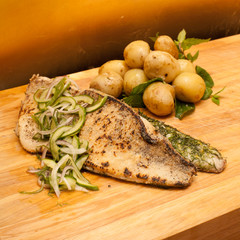 Roasted pike perch with potatoes and pickled cucumber salad. On wooden table.