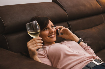Pretty woman talking on mobile and having a glass of while wine while laying at home