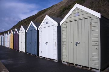 Row of colourful beach huts on beach promenade in front of cliffs
