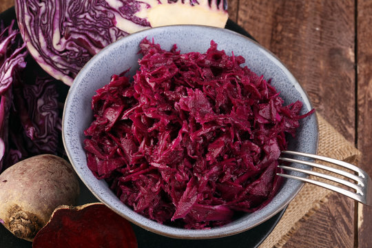 Shredded red cabbage in clay bowl on wooden background. Vegetarian healthy food.