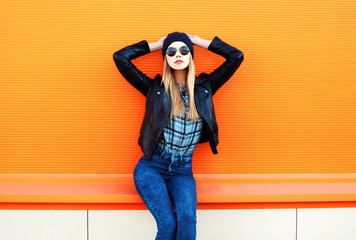 Fashion pretty blonde woman in rock black style posing on a colorful orange background