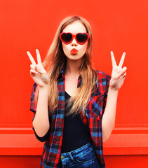 Portrait pretty young woman in red sunglasses shape of heart blowing lips making air kiss outdoors