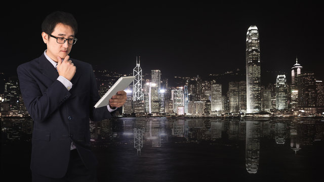 Double exposure Confident Asian businessman reading notebook or document file with cityscape on blurred building.