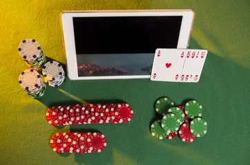 Top view of tablet next to poker chips and cards on green cloth, online poker concept 