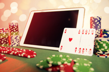 Online poker concept royal flush in cards next to tablet and pile of chips 