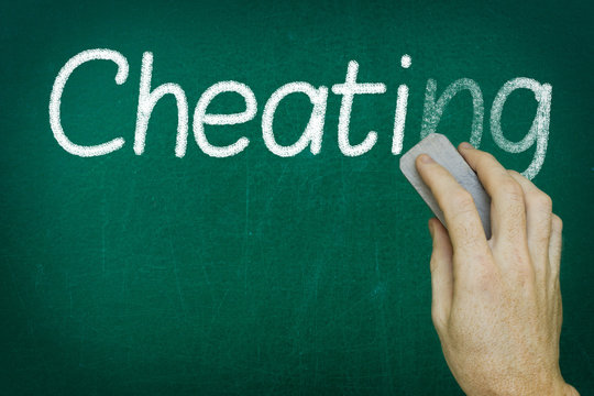 Hand erasing the word CHEATING written on blackboard
