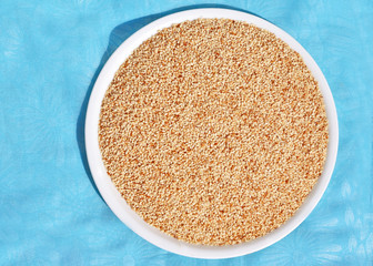 Roasted sesame seeds in white plate on sky blue background.