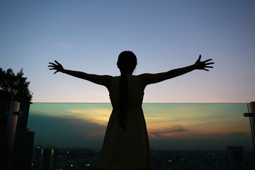 Fototapeta na wymiar Silhouette of woman stretching arms enjoy relax at sunset on rooftop of the building