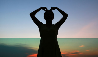 Silhouette of woman expression Heart shape at sunset on rooftop of the building