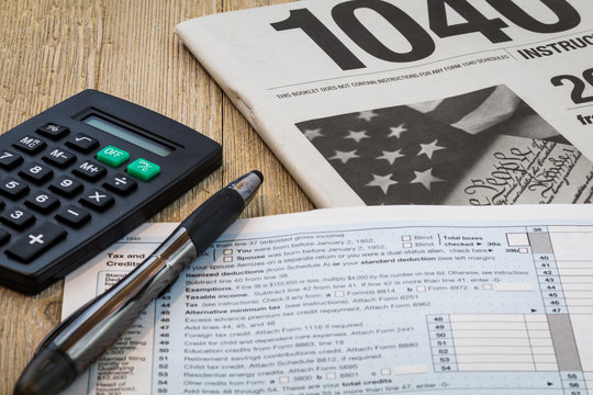 Tax preparation form US 1040 and tax tables, generic (no year specified) with calculator and pen on wooden board