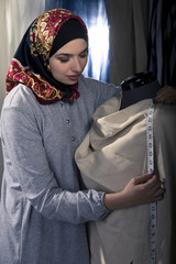 Female fashion designer tailoring conservative clothing in a textile workshop.  The hijab she is wearing is associated with muslims, middle east or eastern european cultures.  