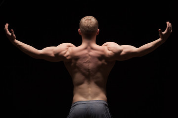Athletic handsome man fitness-model showing his muscular back, isolated on black background with copyspace