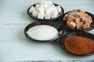 Variety of brown (cane) and white sugar. Granulated and lump sugar in a black small plates. 