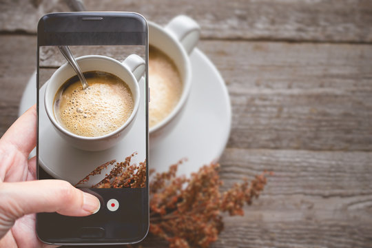 Taking a photo by Finger Pressing on Smartphone for Photograph Close up Hot Coffee on wooden with Copy Space in Chill and Relax Concept, Image for Coffee Advertise or Social Media with Drink Concept