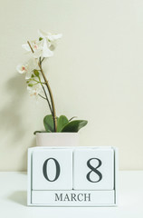 Closeup white wooden calendar with black 8 march word with white orchid flower on white wood desk and cream color wallpaper in room textured background , selective focus at the calendar