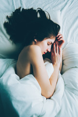 Portrait of young white Caucasian woman lying in bed sleeping, her messy hair on pillow, indoors at home early morning, lifestyle, toned with filters, view from top above