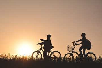 Silhouette of children with bicycle on grass field at the sky sunset, color of vintage tone and soft focus concept journey in holiday