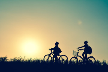 Silhouette of children with bicycle on grass field at the sky sunset, color of vintage tone and soft focus concept journey in holiday