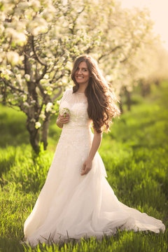 Portrait of the bride in ivory wedding dress with long curly hair walking in gardens with blossom trees like in fairy tale
