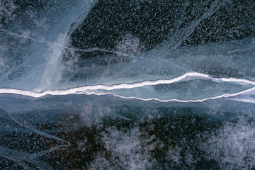 Texture of beautiful fairytale ice of the lake Baikal and cracks on it with snow.