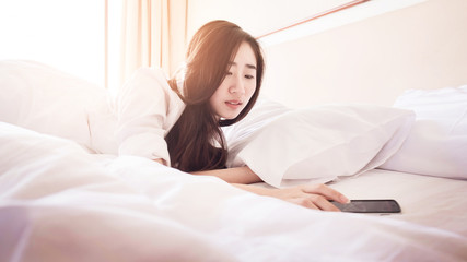 Relaxed woman at home reading a text message on smartphone in her bright bedroom