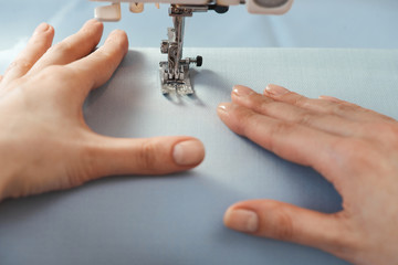 Seamstress threading blue textile on sewing machine close up